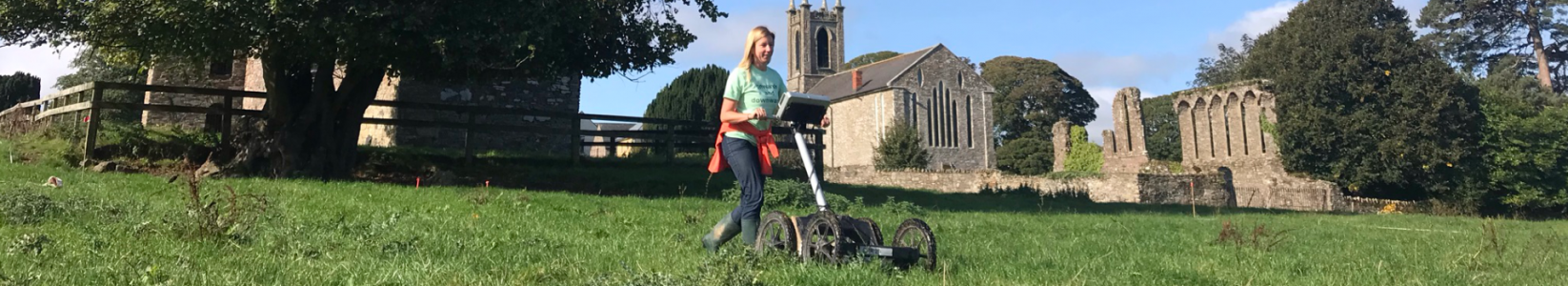 A women uses geophysics equipment to survey an area close to a church.