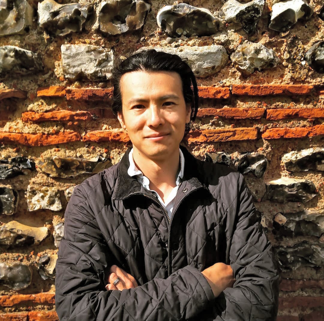 Han Li stands in front of an ancient wall of stone and brick.