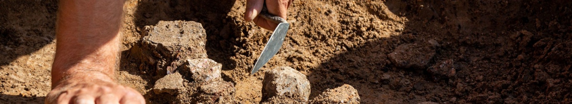 A detail of a trowel being used to excavate and archaeological feature.