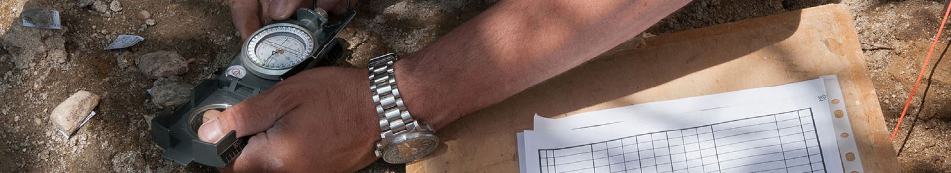 An archaeologist holds a compass whilst recording an archaeological feature.