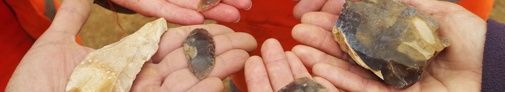 Hands holding flint tools are held together in a circle.