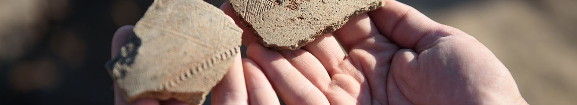Hands hold two fragments of ancient pottery with incised decoration.