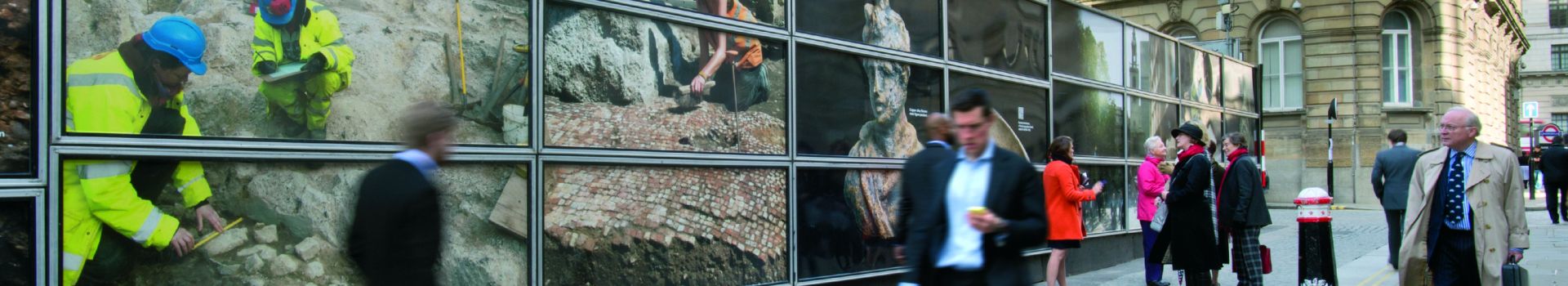 People in suits walking past hoardings with images of archaeologists