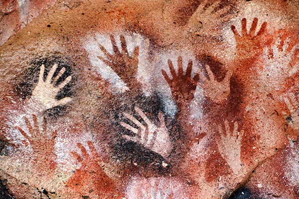 Ancient stencilled hand prints surrounded by black and orange dye on a cave wall.