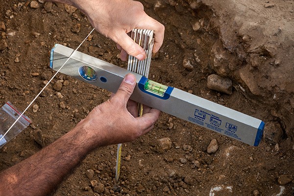 Hands hold a spirit level and ruler whilst recording an archaeological feature.