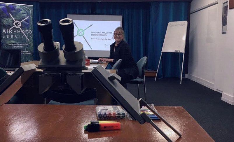 A woman sits at a desk in front of equipment.