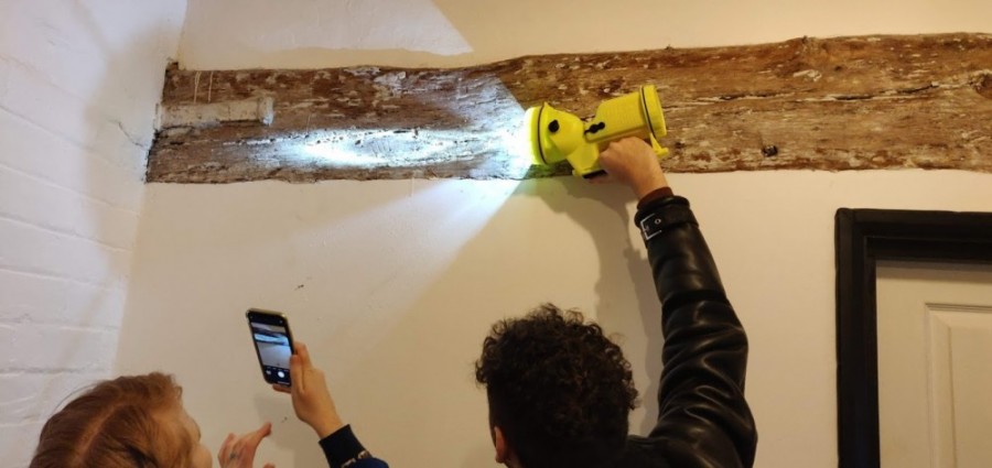 A torch is shone on an old wooden beam in a building.
