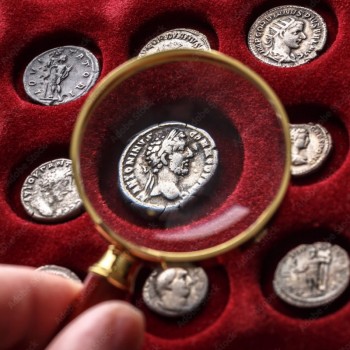 A magnifying glass examines a Roman coin.