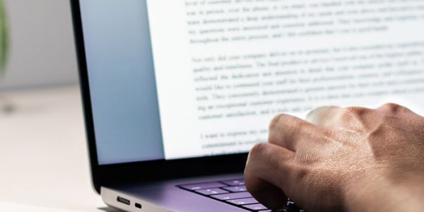 A person sits at a desk and types on a laptop next to a desk lamp.