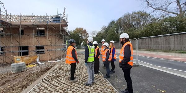 Archaeologists in hard hats and hi-vis clothing are tutored on a construction site.