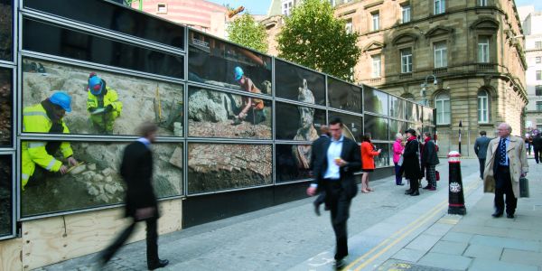 People in suits walking past hoardings with images of archaeologists