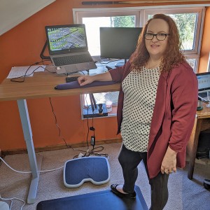 Sarajayne Clements stands in front of a desk with computer.