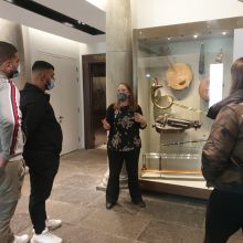 A person talks to a small group of people next to museum cases containing artefacts.